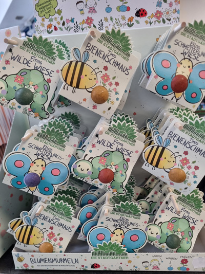 Bunte Samenverpackungen mit Insektenmotiven, beschriftet als „Bienenschmaus“ und „Wilde Wiese“.