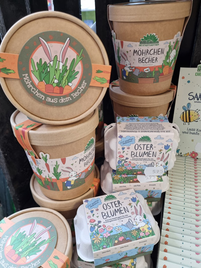 Dekorative Gartenprodukte mit frühlingshaften Designs, darunter Möhrchenbecher und Oster-Blumen-Kartons.