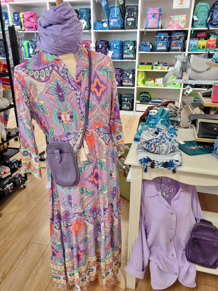 Eine Schaufensterpuppe trägt ein buntes Kleid mit floralen Mustern, lila Tasche und Kopftuch.