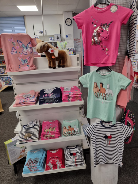Ein Regal mit bunten Kinder-T-Shirts und einem flauschigen Spielzeugpferd in einem fröhlichen Geschäft.