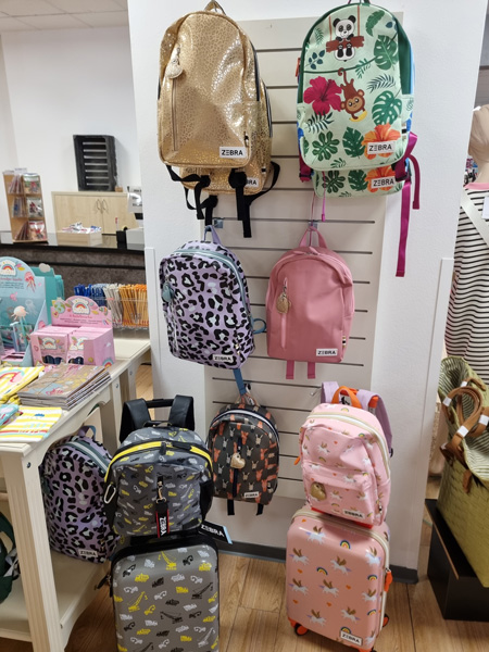 Bunte Rucksäcke mit verspielten Designs hängen in einem Geschäft an einer weißen Wandhalterung.