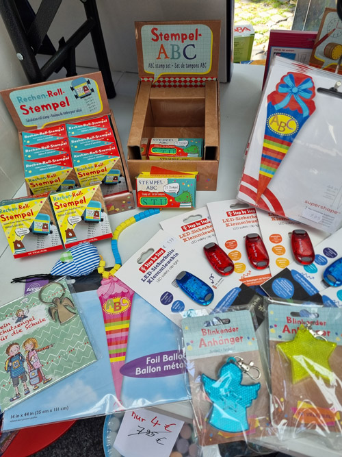 Bunte Bastel- und Schreibwaren auf Marktstand, darunter Stempelsets, blinkende Anhänger und Folienballons.