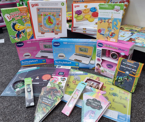 Bunte Lernspielzeuge und Schulartikel für den Schulstart, darunter Bücher, Stifte und ein Lerncomputer.