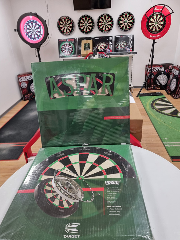 Ein Raum mit mehreren Dartboards und zwei großen grünen Kartons mit der Aufschrift "ASPAR".