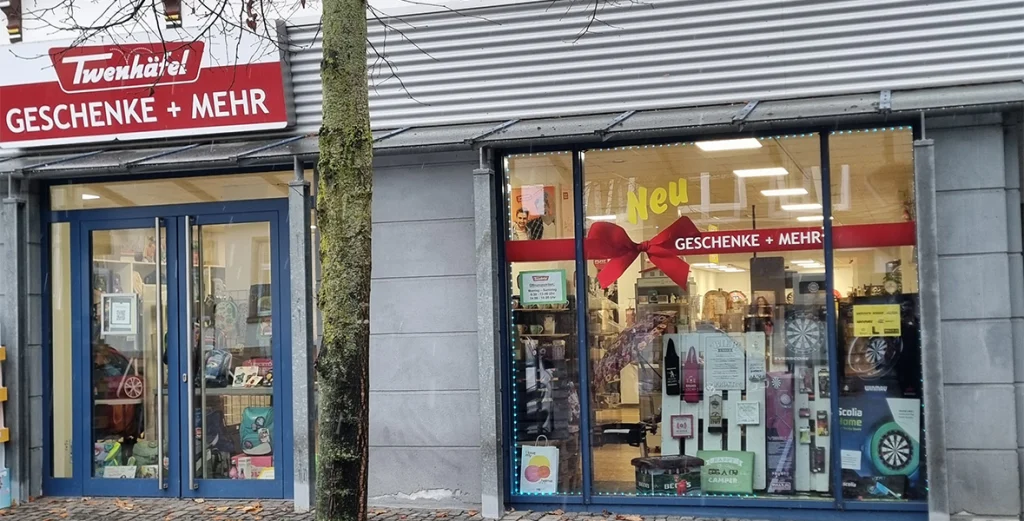 Ladenfassade von "Twenhäfel GESCHENKE + MEHR" mit rotem Schild und großer Schleife im Schaufenster.