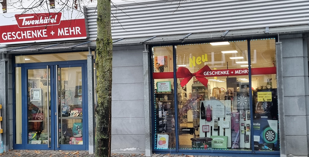 Ladenfassade von "Twenhäfel GESCHENKE + MEHR" mit rotem Schild und großer Schleife im Schaufenster.