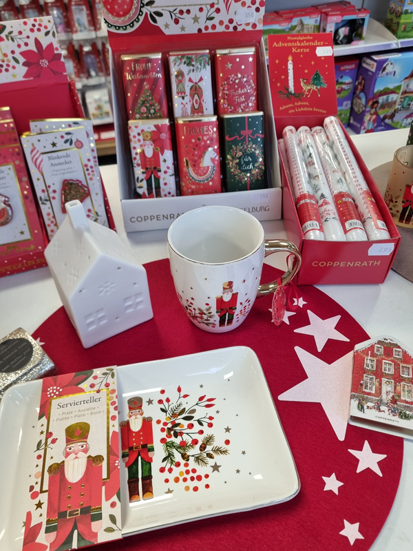 Weihnachtliche Verkaufsauslage mit Tassen, Schokolade, Adventskerzen und einem dekorativen Häuschen.