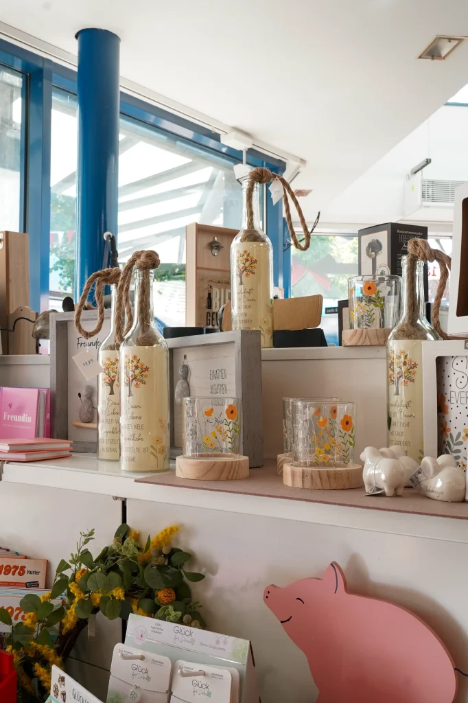 Dekorative Auslage mit Flaschen, Gläsern und einem rosafarbenen Holzschwein in sanften Farben.