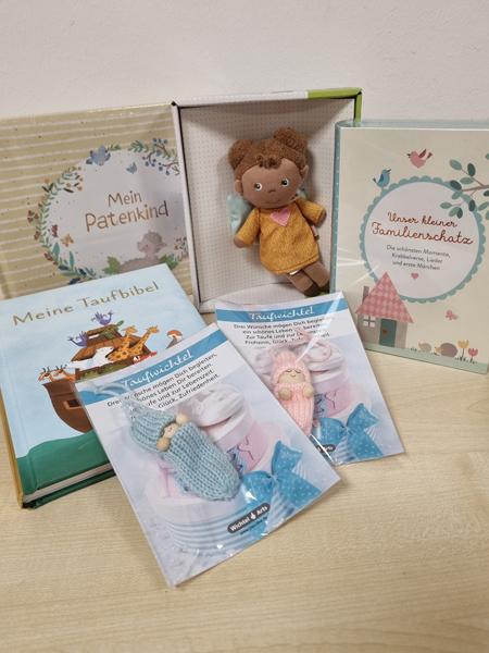 Eine Sammlung von Taufgeschenken, darunter Bücher, Taufkerzen und eine Stoffpuppe in sanften Farben.