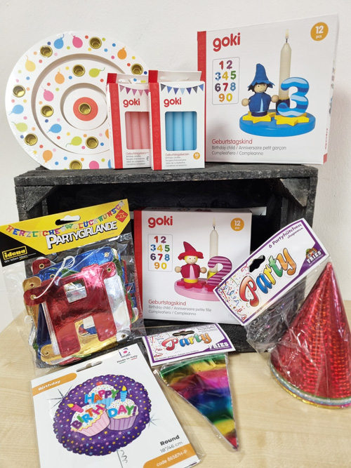 Bunte Geburtstagsartikel auf einem Tisch, darunter Kerzen, Partyhüte und Pappteller, für eine Feier.