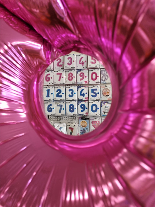 Ein pinker Ballonrahmen zeigt bunte Zahlenverpackungen an einer Wand, festliche Atmosphäre.