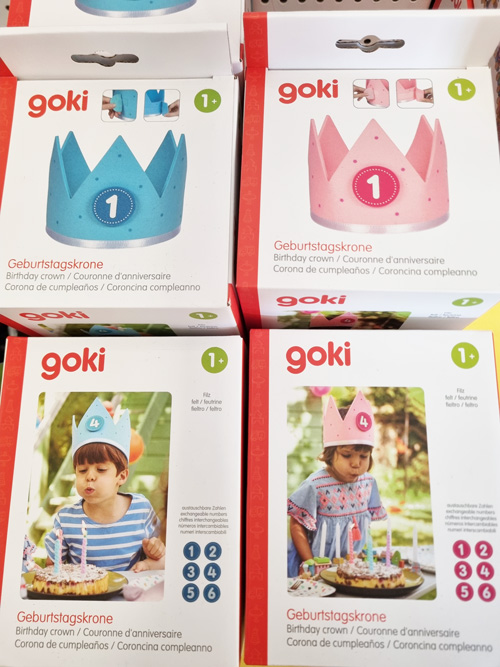 Vier bunte Geburtstagskronen-Verpackungen von goki, mit fröhlichen Kindern und Zahlen 1 und 4.