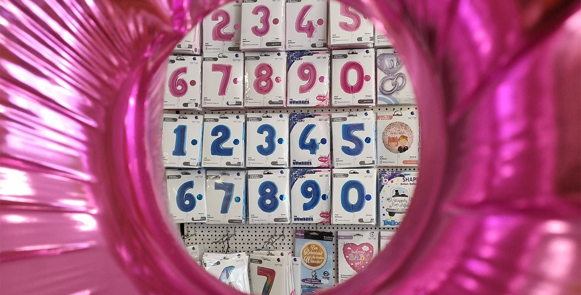 Ein pinker Ballonrahmen zeigt eine Wand mit rosa und blauen Zahlenballon-Verpackungen in einem Geschäft.