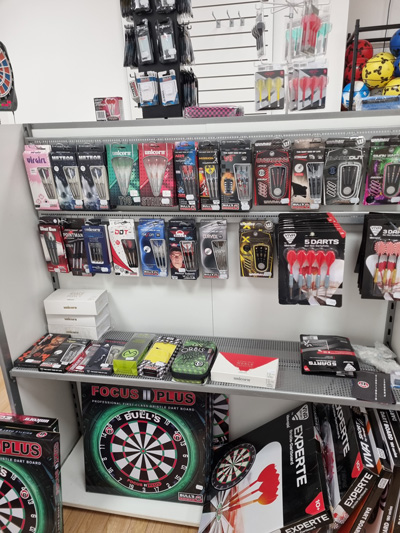 Ein Regal in einem Dartgeschäft zeigt Dartpfeile, Flights und Dartboards in verschiedenen Farben und Designs.