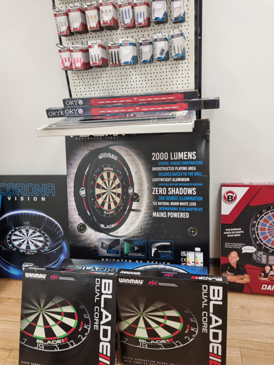 Dartzubehör im Geschäft: Dartboards, Flights und Beleuchtung, ordentlich präsentiert in kräftigen Farben.