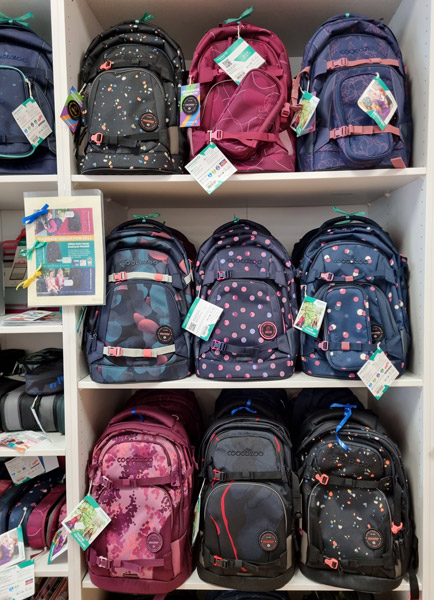 Ein Regal zeigt bunte Schulrucksäcke in verschiedenen Designs und Farben, bereit zum Verkauf.
