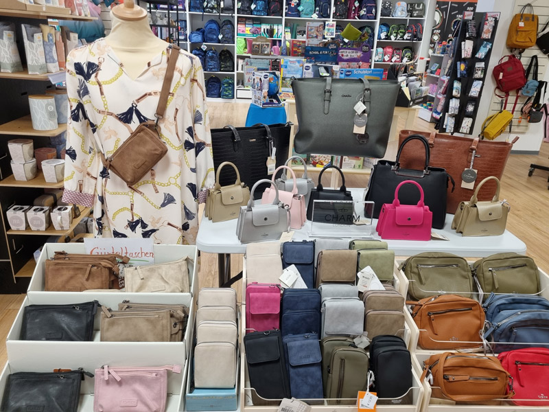 Ein Geschäft zeigt Taschen und Accessoires, mit einer Schaufensterpuppe in gemusterter Bluse.