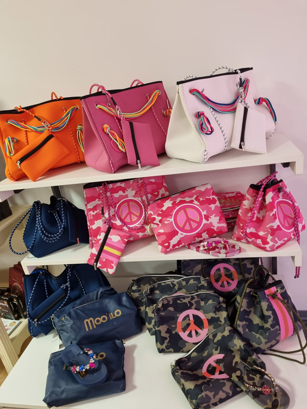 Verschiedene bunte Taschen auf Regalen, von leuchtenden bis dunklen Tönen, in einem Geschäft ausgestellt.