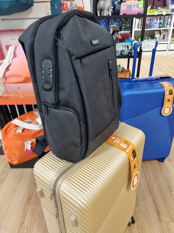 Ein schwarzer Rucksack und zwei Hartschalenkoffer in Beige und Blau sind in einem Geschäft ausgestellt.