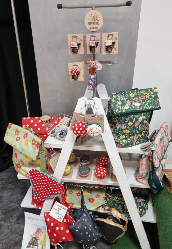 Ein bunter Verkaufsstand zeigt Fahrradtaschen mit Blumenmustern und Accessoires wie glänzende Klingeln.