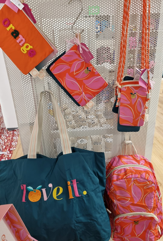 Bunte Taschen und Accessoires auf Metallständer, fröhliche Designs in Orange, Pink und Dunkelblau.