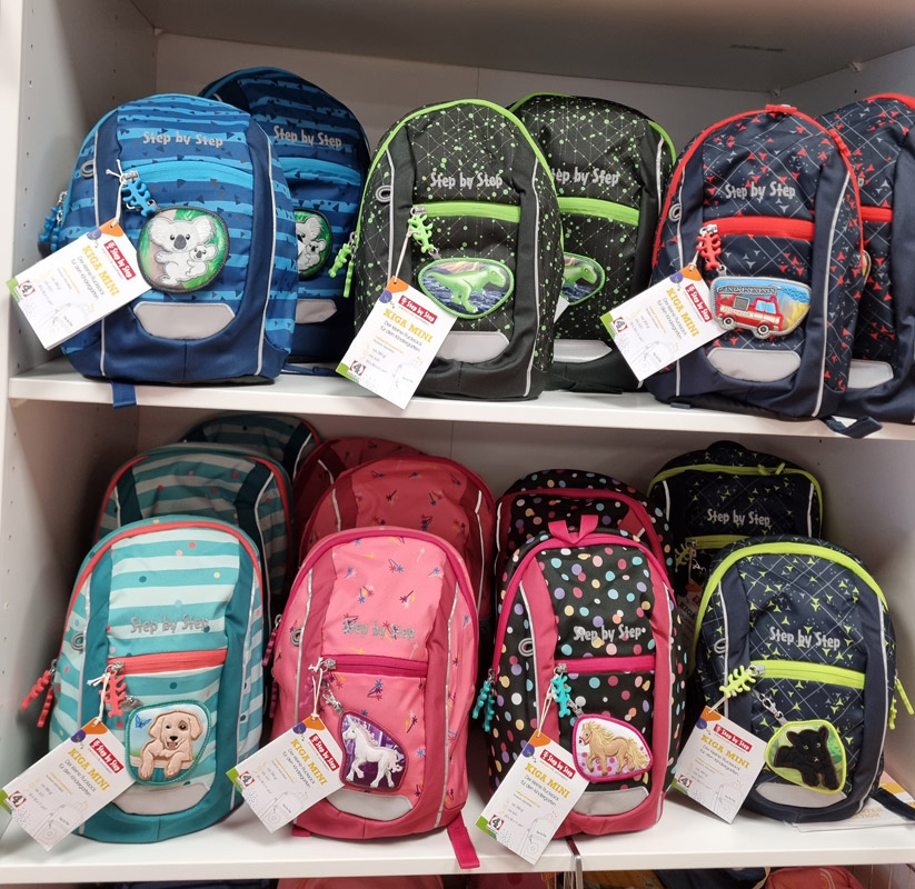 Ein Regal voller bunter Kinderrucksäcke in verschiedenen Designs und Farben in einem Geschäft.