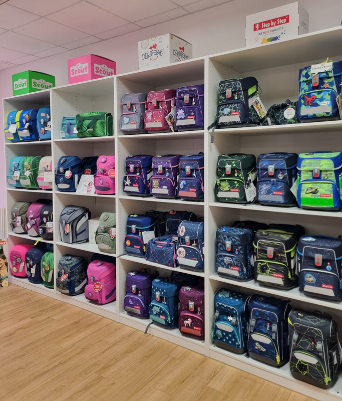 Ein Regal voller bunter Schulranzen in verschiedenen Farben und Designs in einem Fachgeschäft.